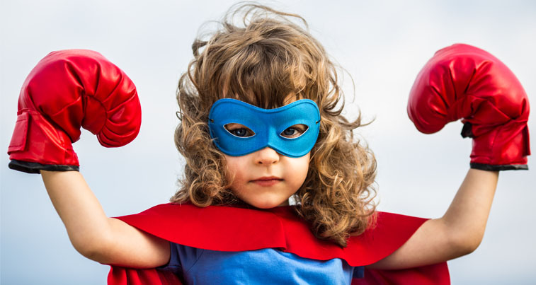 Young girl with tawny curly hair, a blue super hero mask and red boxing gloves with her arms raised up in a muscles position